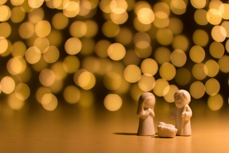 Mary, Joseph, and baby Jesus figurines in front of Christmas lights.