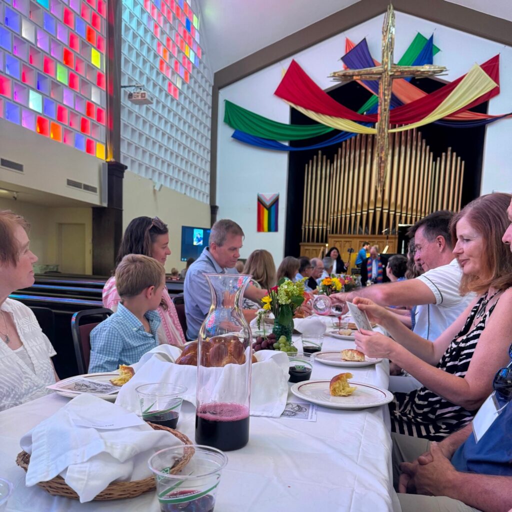 Congregants sitting at a long dining table in the sanctuary, eating and taking communion