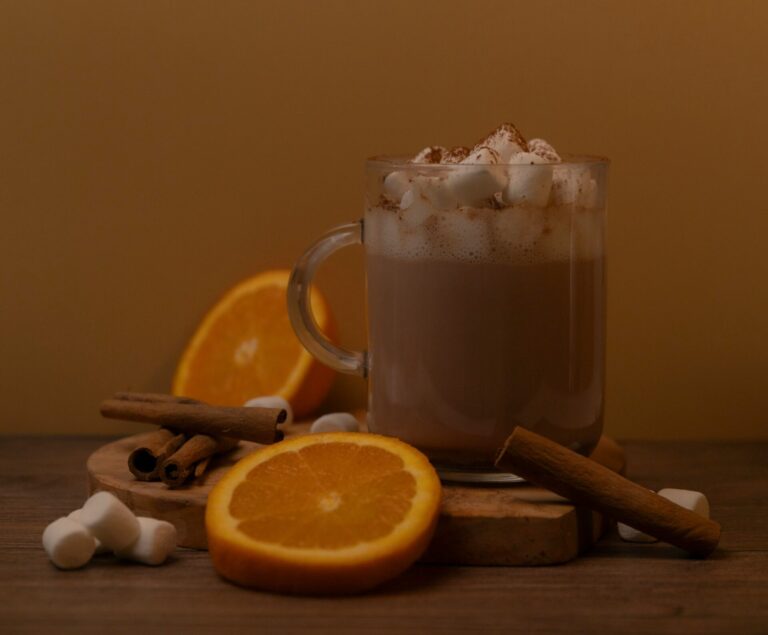 Mug of hot cocoa with marshmallows, surrounded by orange slices and cinnamon sticks