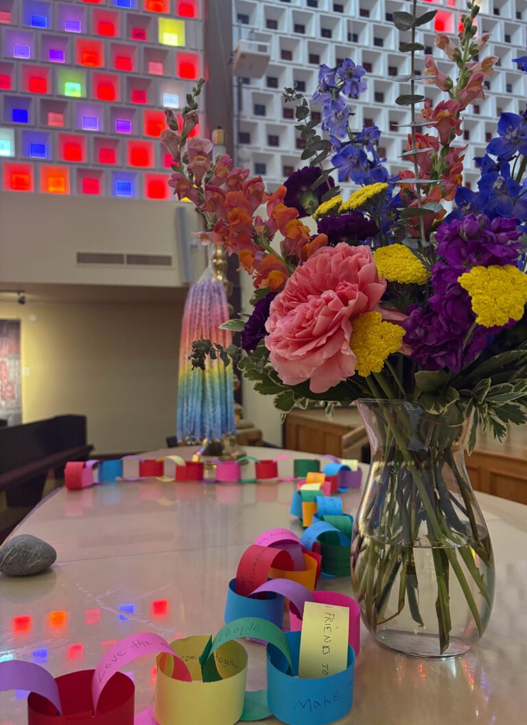 Paper chain and flowers on the altar with rainbow origami and windows in the background.