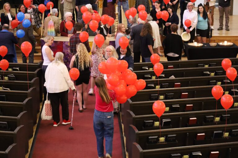 Members of First Church gathered in the aisle with red balloons