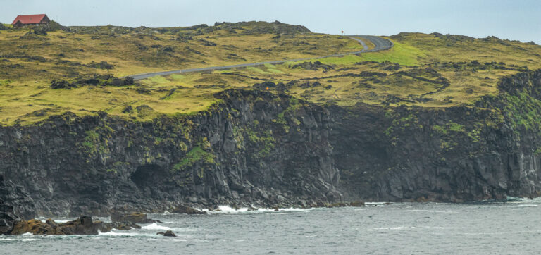 Photo of a cliff in Iceland with an empty road and a single house