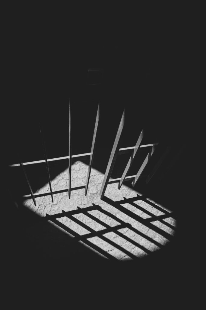 Black and white photo of light shining through prison bars