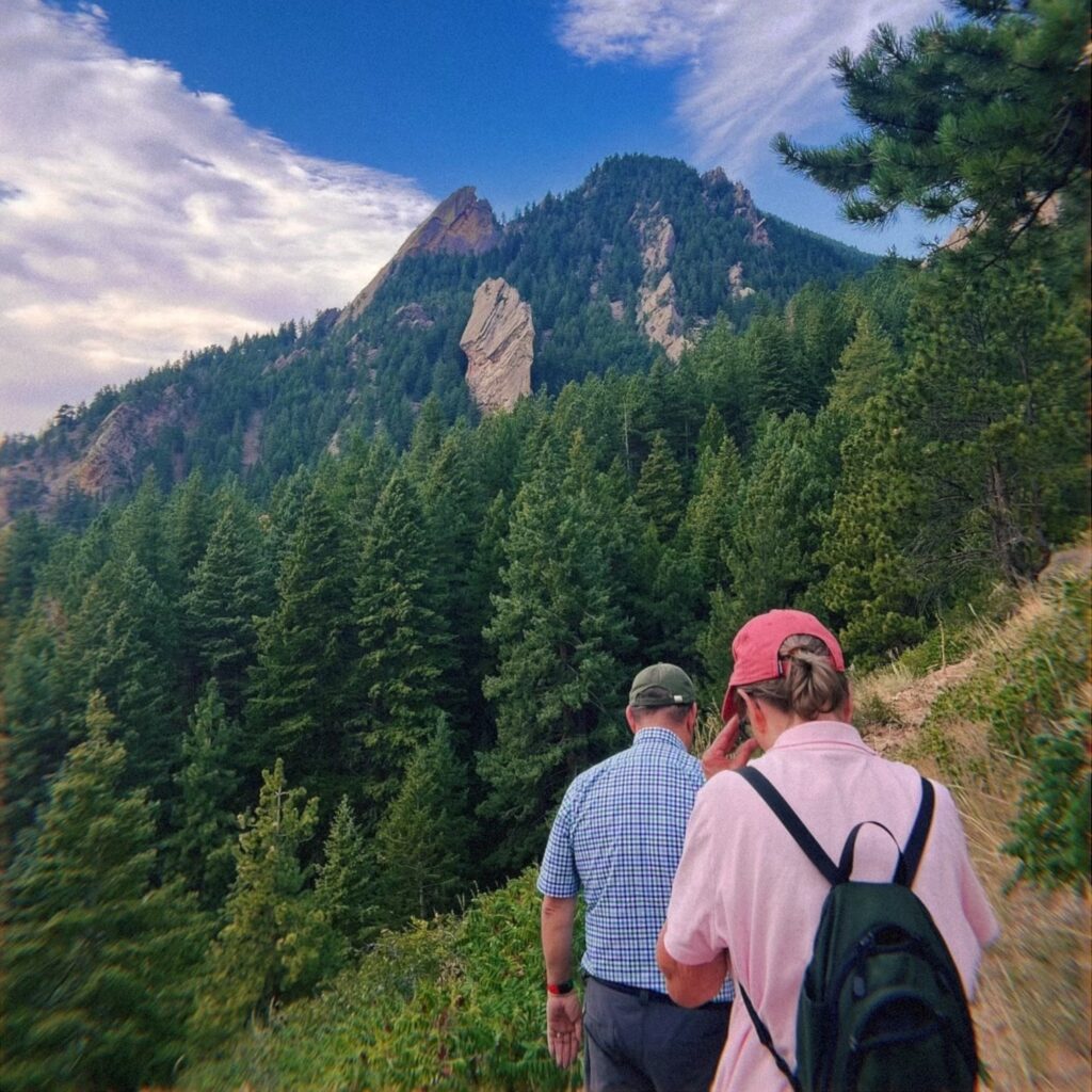 Two people hiking with evergreen trees and mountains in the background