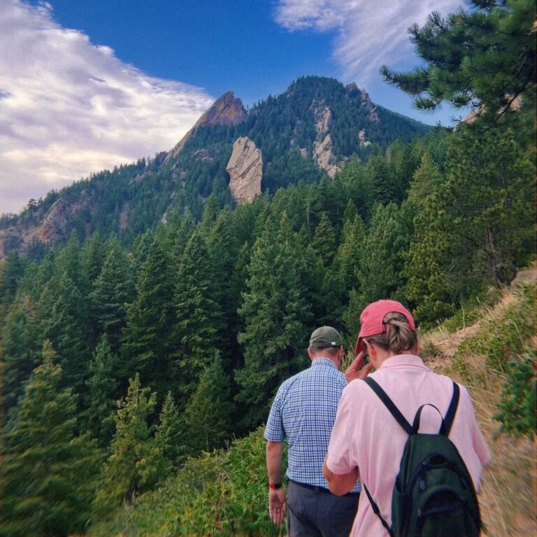 Two people hiking with evergreen trees and mountains in the background