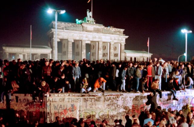 Image of people standing atop the Berlin Wall at night