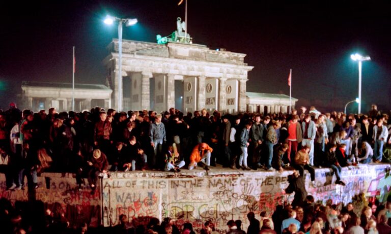Image of people standing atop the Berlin Wall at night